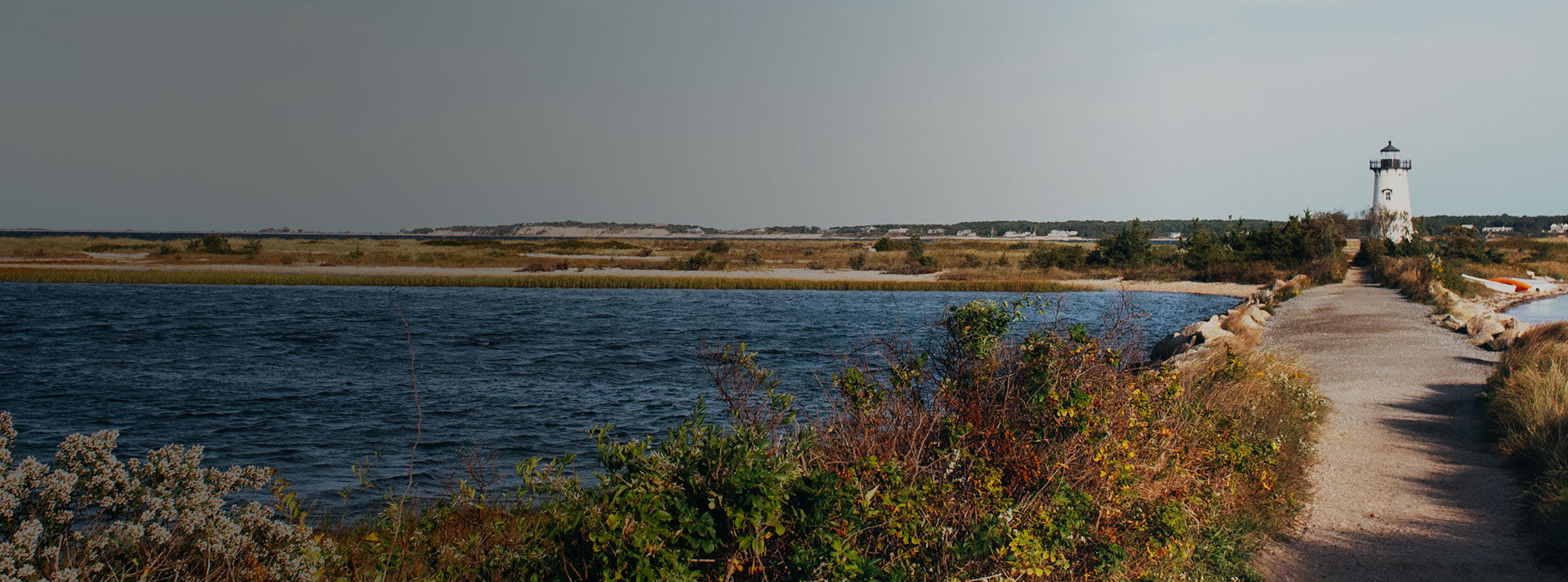 A scenic photograph of Edgartown Lighthouse on Martha's Vineyard, framed on the left by foliage and the ocean.